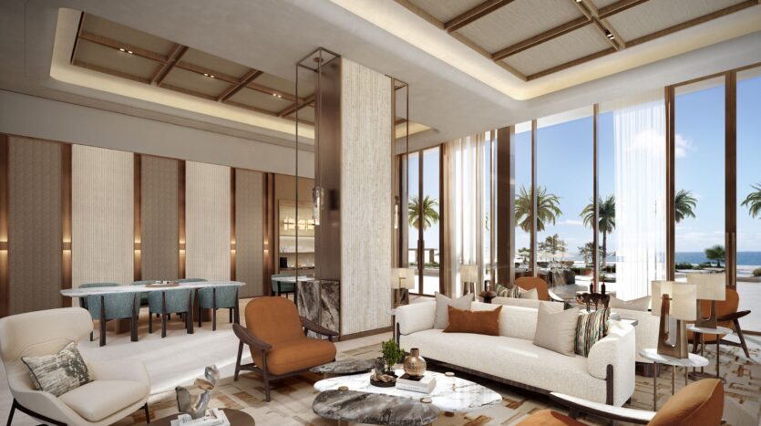 The luxurious and modern lounge at the Four Seasons Private Residences features elegant sofas and armchairs, as well as marble tables. Large windows offer glimpses of palm trees and ocean views, while soft lighting and neutral tones create a serene and welcoming atmosphere.