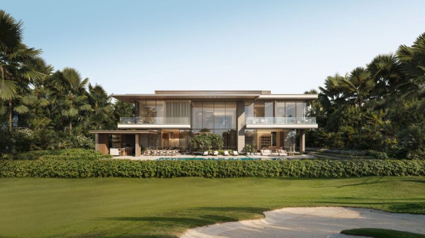 A modern two-story villa at Four Seasons Private Residences, featuring large floor-to-ceiling windows and surrounded by lush palm trees and greenery, boasts a swimming pool and an outdoor seating area overlooking a manicured lawn and a sand bunker beneath a clear blue sky.