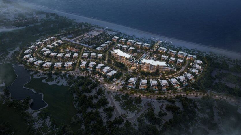 A nighttime aerial view of Four Seasons Private Residences, a large beachfront resort complex consisting of several modern buildings surrounded by trees and greenery, situated along a picturesque coastline and connected by walking paths.