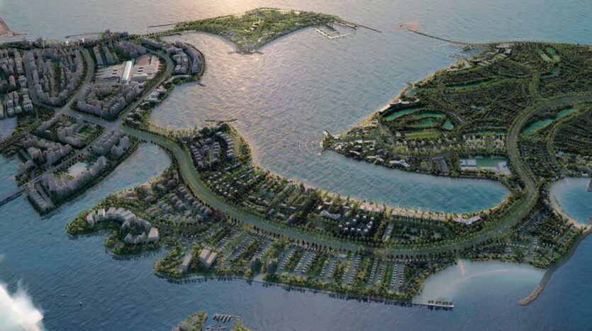 Vue aérienne d'une ville côtière avec des espaces verts, des routes sinueuses et des résidences Meriden Beach sur plusieurs îles entourées d'eau, reliées par des ponts, sous un soleil couchant.