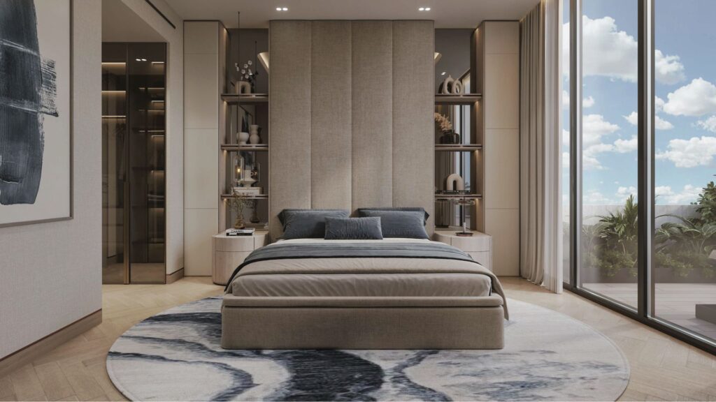 Chambre à coucher moderne aux Résidences Meriden Beach avec un grand lit rembourré, une literie grise et beige, des étagères encastrées, une fenêtre allant du sol au plafond et montrant un ciel bleu, et un tapis à motifs ronds sur un sol en bois. La décoration est minimaliste et dans des tons neutres.
