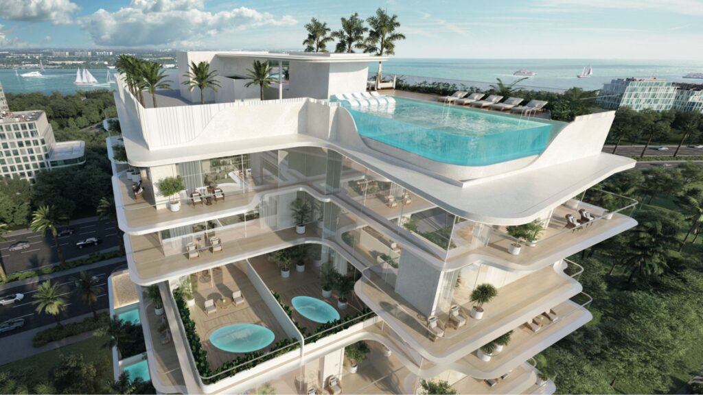 Le Meriden Beach Residences est un immeuble moderne d'appartements de luxe en bord de mer, doté de balcons spacieux, de jacuzzis privés et d'une piscine à débordement sur le toit, entourée de palmiers, avec une vue imprenable sur l'océan et les bateaux au loin.