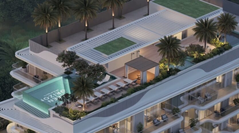 Le toit moderne des Meriden Beach Residences comprend une piscine à débordement aux parois de verre, des chaises longues, des palmiers, des pelouses vertes et un coin salon ombragé au sommet d'un immeuble d'appartements contemporain doté de grands balcons.