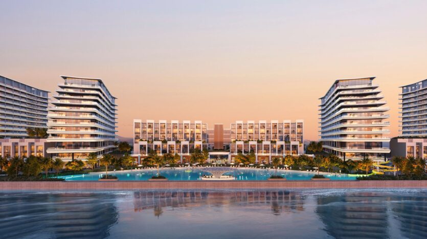 River Cove Residences, a modern waterfront complex featuring multi-story buildings, palm trees, and a crystal-clear pool at sunset. The buildings are reflected in the water as the sky glows with warm shades of orange and pink.