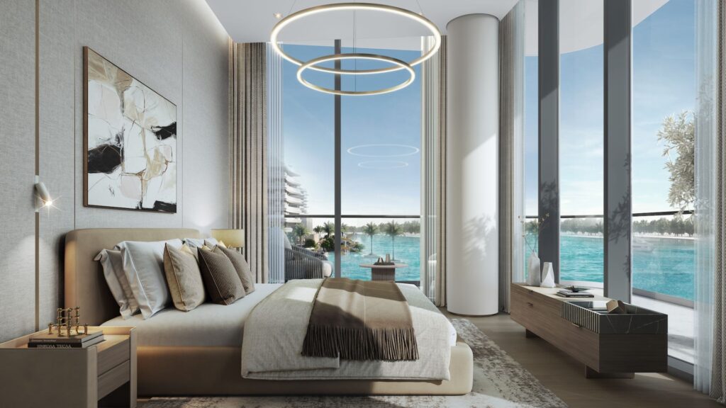 A modern bedroom at River Cove Residences featuring floor-to-ceiling windows overlooking the blue waterfront, a beige bed with plenty of pillows, abstract wall art, circular ceiling lights, and minimalist wooden furniture.