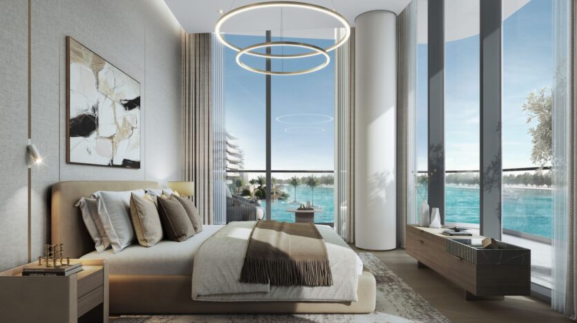 A modern bedroom at River Cove Residences featuring floor-to-ceiling windows overlooking the blue waterfront, a beige bed with plenty of pillows, abstract wall art, circular ceiling lights, and minimalist wooden furniture.