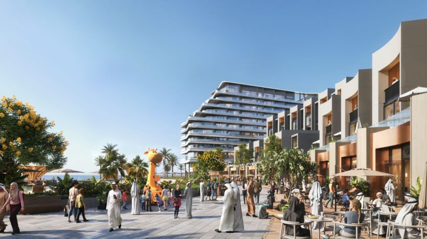 The lively outdoor plaza at River Cove Residences is a gathering spot for strollers, coffee shops, and a large giraffe-shaped playground. Modern apartments and palm trees line the area under a clear blue sky.