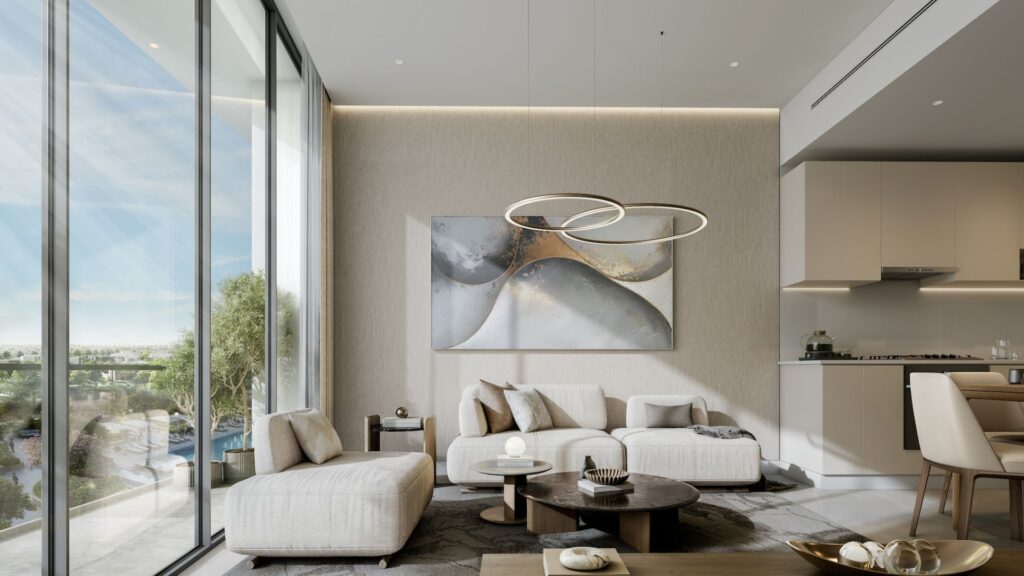 A modern living room at River Cove Residences featuring floor-to-ceiling windows, light beige sofas, a round coffee table, abstract wall art, and a contemporary ring-shaped chandelier. The outdoor greenery is visible through the windows; the kitchen is partially visible on the right.