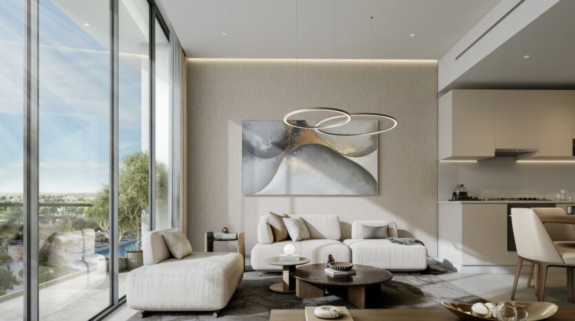 A modern living room at River Cove Residences featuring floor-to-ceiling windows, light beige sofas, a round coffee table, abstract wall art, and a contemporary ring-shaped chandelier. The outdoor greenery is visible through the windows; the kitchen is partially visible on the right.