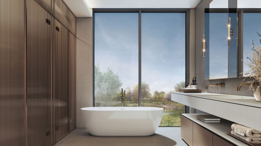 Modernes Badezimmer im „The Orchard by Sobha“ mit einer freistehenden weißen Badewanne, raumhohen Fenstern, eingebauten Holzschränken, einem Doppelwaschbecken mit Spiegel und sanftem Tageslicht, das den Raum erhellt.
