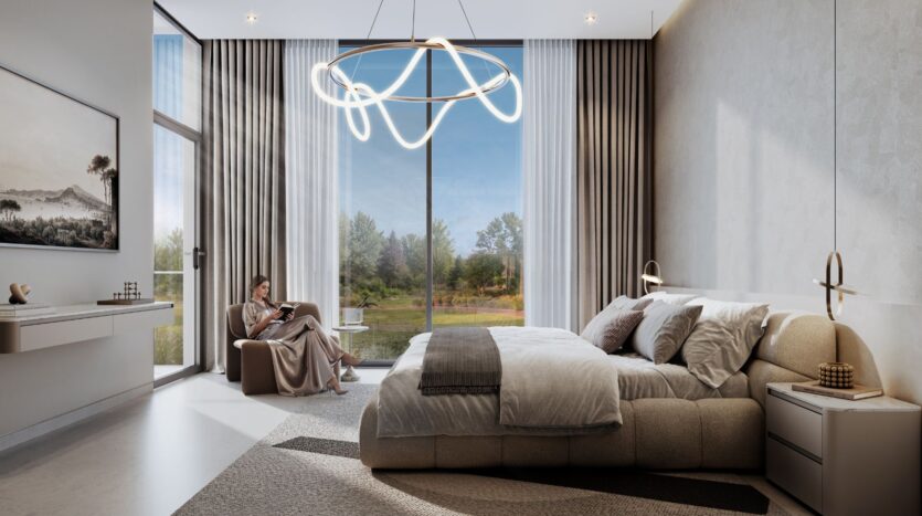 A modern bedroom at The Terraces by Sobha features a king-size bed, neutral tones, and floor-to-ceiling windows. A woman is reading by the window, beneath a unique circular chandelier, with a view of the trees and sky outside.