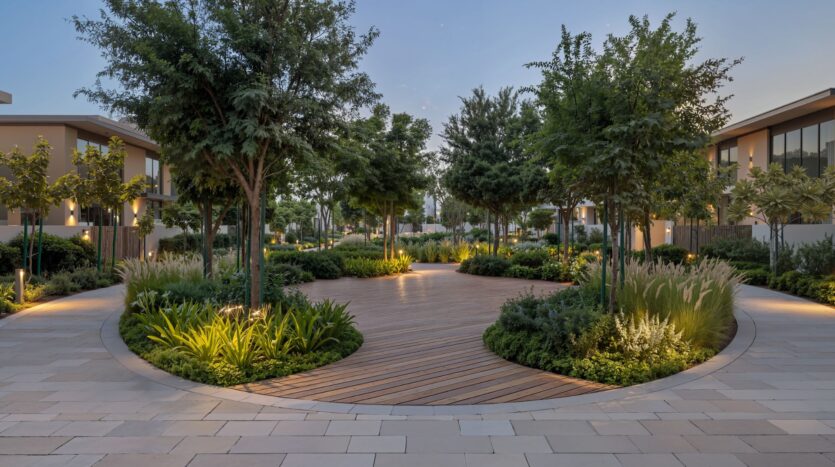 A circular wooden walkway surrounded by lush greenery and trees at The Terraces by Sobha, nestled among modern buildings at dusk, with soft outdoor lighting creating a peaceful atmosphere.