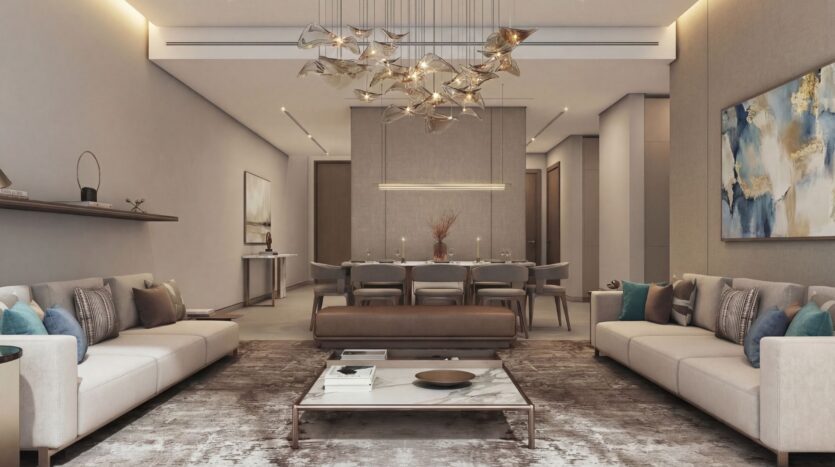 An elegant, modern living room at The Terraces by Sobha, featuring neutral tones, two beige sofas, a marble coffee table, an abstract chandelier, a large rug, wall art, and a dining area. Soft, warm lighting creates a cozy atmosphere.