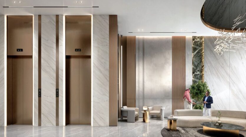 The modern and luxurious lobby of Tides by Amis, featuring marble floors and walls, two elevators, elegant seating, a round table, a large potted plant, and two men in conversation—one in a suit, the other in traditional Middle Eastern attire.