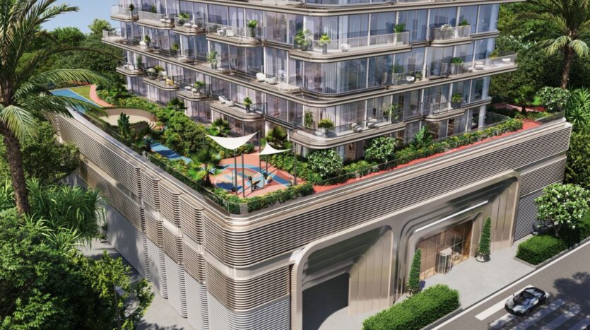 A modern multi-story building, The Tides by Amis hotel features glass balconies and terraces with lush greenery. The rooftop offers a swimming pool, shaded seating areas, and gardens. Trees surround the building as a car drives past the entrance below.