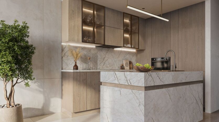 A modern kitchen featuring light wood cabinets, glass upper shelves, marble countertops and an island, a built-in oven, under-cabinet lighting, and a potted plant in the corner. A bowl of green apples evokes the serene atmosphere of The Tides by Amis.