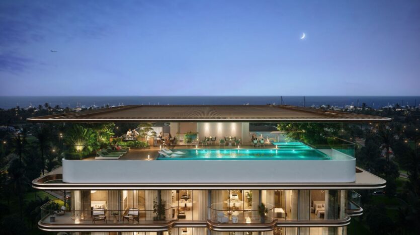 At dusk, the modern tower The Tides by Amis features a rooftop infinity pool surrounded by lounge chairs and lush greenery. Its open-air design offers breathtaking views of the city and the ocean under a twilight sky with a crescent moon.