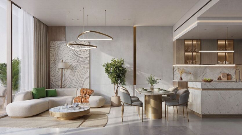 Modern open-concept living room and kitchen in The Tides by Amis, featuring neutral tones, gold accents, a round sofa, a marble coffee table, a houseplant, pendant lights, a dining table with chairs, and floor-to-ceiling windows that flood the space with natural light.