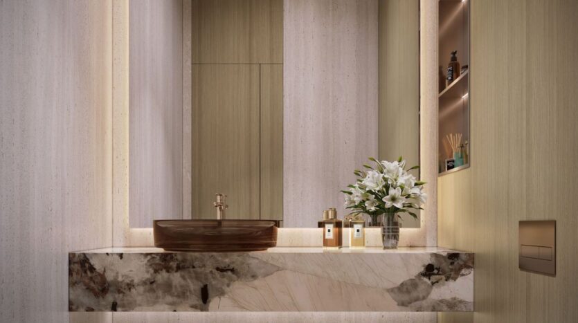 A modern bathroom featuring a marble countertop, a brown glass sink, and a gold faucet. A copy of *The Tides* by Amis sits next to a vase of white lilies, perfume bottles, and toiletries, bathed in soft ambient lighting.