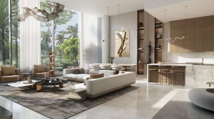 A modern, spacious living room with large windows, neutral-toned furniture, a marble kitchen island, abstract artwork, and views of lush greenery—all of which perfectly complement the serene atmosphere of The Tides by Amis—is visible through sheer white curtains.