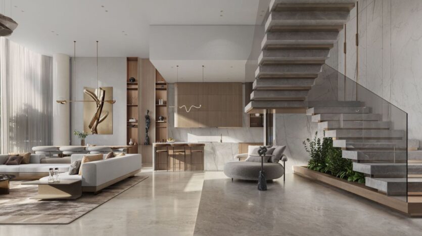 A spacious, modern living room with large windows, light gray furniture, marble floors, and a floating staircase with a glass railing—The Tides by Amis features built-in wooden shelves and minimalist decor bathed in soft natural light.