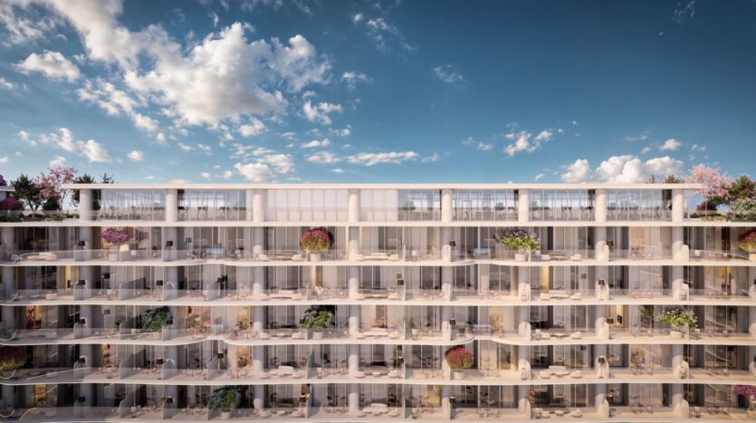 La Wow Tower est un bâtiment moderne de plusieurs étages avec des balcons en verre et des plantes en pot à chaque niveau, vue de face sur un ciel bleu avec des nuages épars.