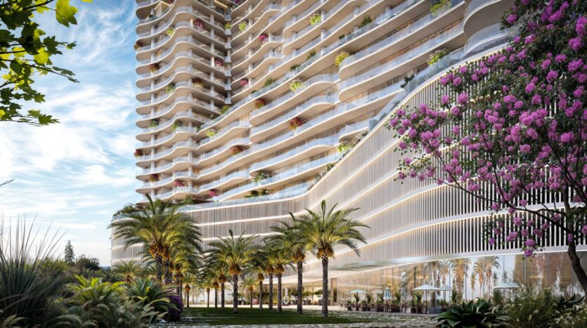 La Wow Tower est une tour moderne avec des balcons incurvés, une végétation luxuriante et des plantes à fleurs. Des palmiers et des jardins paysagers entourent sa base, avec de grandes fenêtres et des sièges extérieurs sous un ciel bleu parsemé de nuages.
