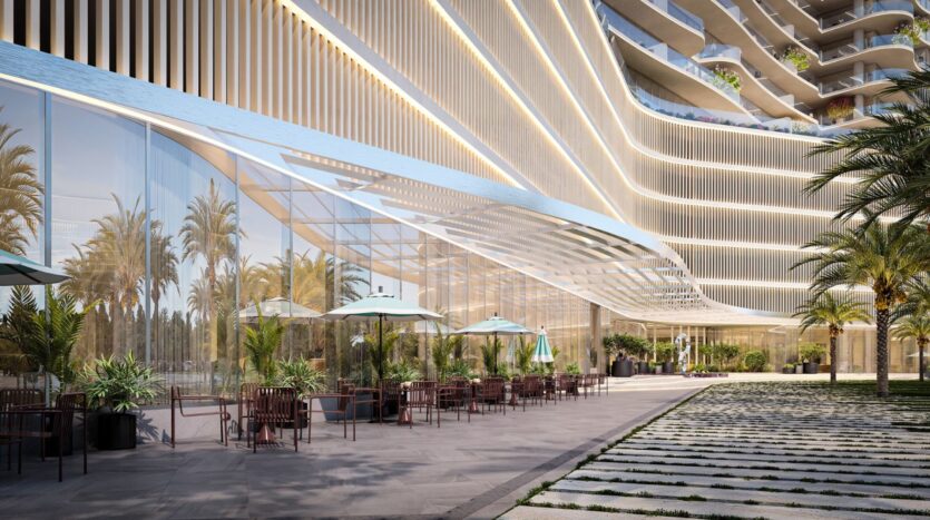 Terrasse extérieure avec tables, chaises et parasols à côté du bâtiment moderne en verre de la Wow Tower, avec des palmiers, des plantes en pot et des lignes architecturales ondulées sous un ciel clair.