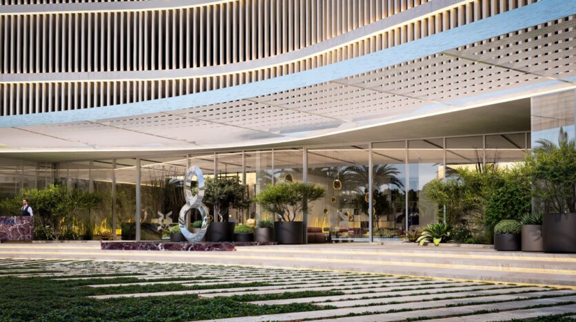 Entrée moderne de l'immeuble The Wow Tower avec de grandes baies vitrées, un auvent métallique incurvé, un éclairage décoratif, des plantes en pot, une sculpture contemporaine et un aménagement paysager soigné au premier plan.
