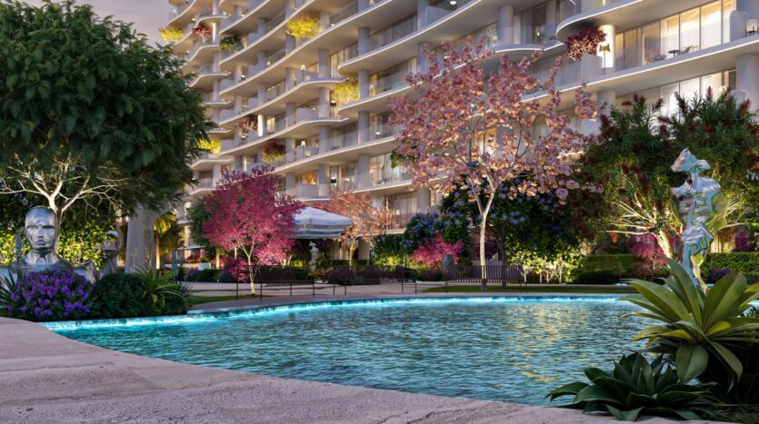 Une piscine entourée d'arbres luxuriants, de plantes à fleurs colorées et de statues se trouve devant l'immeuble d'appartements moderne de la Wow Tower, avec des balcons incurvés et de la verdure. Un éclairage doux crée une atmosphère paisible et accueillante.
