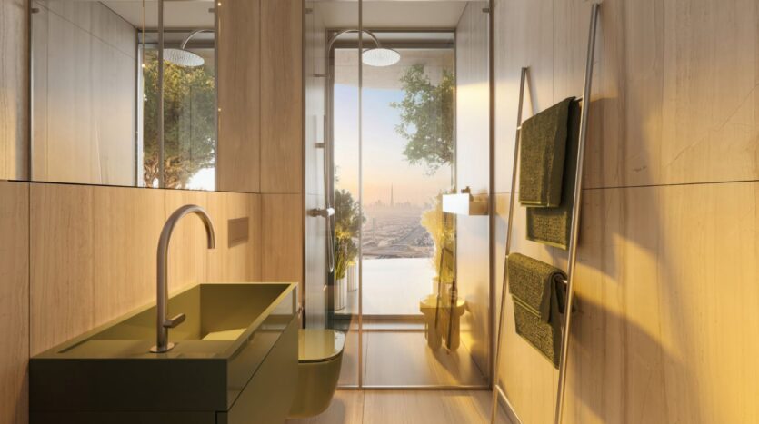 Salle de bains moderne avec lavabo et toilettes verts, murs en bois clair, porte-serviettes avec des serviettes vertes, et une grande fenêtre donnant sur la Wow Tower au coucher du soleil. La douche est équipée d'un pommeau de douche à effet de pluie et offre une vue sur l'arbre à l'extérieur.