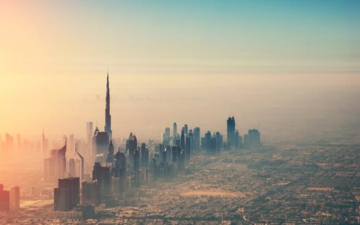 An aerial view of Dubai’s skyline at sunrise, with the Burj Khalifa towering above the other skyscrapers—a striking sight that reflects the growth shown in Dubai’s real estate market figures for March 2026 as the city stretches toward a misty, golden horizon.
