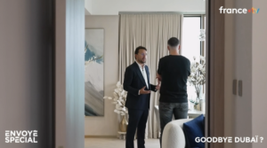 Dos hombres están de pie en un salón moderno, en plena conversación; uno lleva gafas, el otro va vestido de manera informal. En la pantalla aparecen los títulos «Envoyé Spécial» y «Goodbye Dubaï?» —vea la repetición del programa «Envoyé Spécial» sobre la agencia Dubai Immo en France TV.