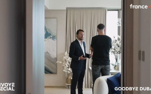 Zwei Männer stehen in einem modernen Wohnzimmer und unterhalten sich; der eine trägt eine Brille, der andere ist leger gekleidet. „Envoyé Spécial“ und „Goodbye Dubaï?“ erscheinen auf dem Bildschirm – sehen Sie sich die Aufzeichnung der Sendung „Envoyé Spécial“ über die Agentur Dubai Immo auf France TV an.