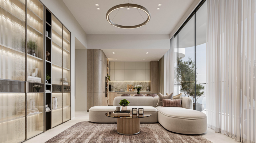 Un salon moderne avec un canapé blanc incurvé, une table basse ronde et des étagères ouvertes doucement éclairées. De grandes fenêtres allant du sol au plafond avec des rideaux transparents inondent l'espace de lumière. Le coin cuisine et l'œuvre d'art Cybele by Wadan sont visibles à l'arrière-plan.