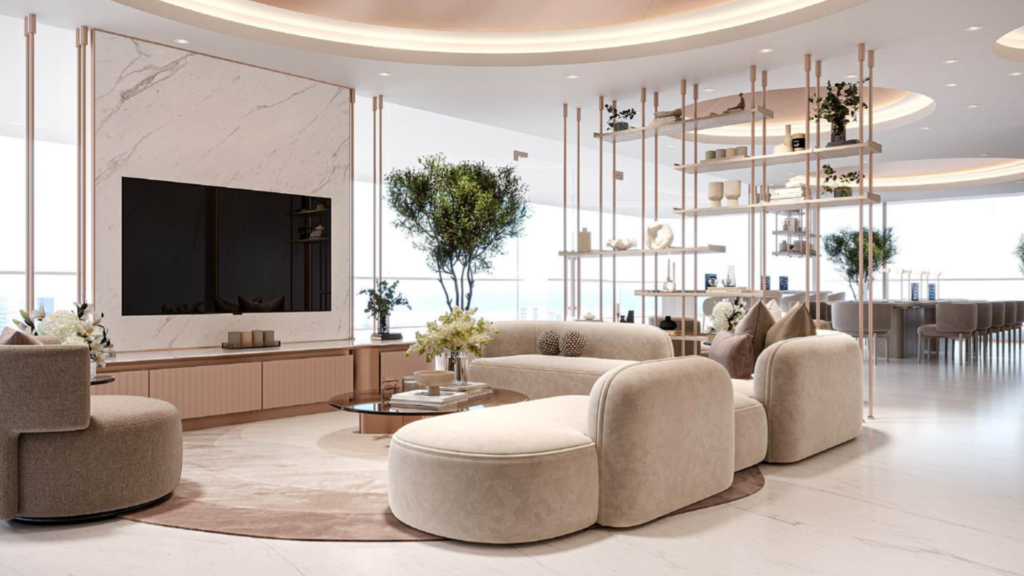 Le salon moderne et spacieux est composé de canapés beiges incurvés, d'une table basse ronde et de l'œuvre d'art Cybele by Wadan au-dessus de la grande télévision sur un mur en marbre. Il est complété par des étagères minimalistes, des plantes d'intérieur et des fenêtres allant du sol au plafond qui baignent l'espace de lumière.