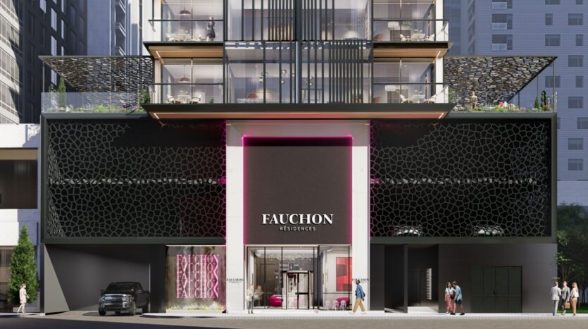 Extérieur d'un bâtiment moderne avec une façade géométrique noire, une grande enseigne indiquant "Résidence Fauchon", une entrée vitrée et des espaces commerciaux au niveau de la rue. Des personnes et une voiture garée sont visibles devant la résidence Fauchon.