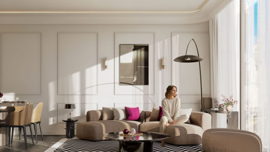 Une femme est assise sur un canapé beige moderne dans le salon lumineux et stylé de la résidence Fauchon, doté de grandes fenêtres, de murs neutres, d'un lampadaire noir et de coussins d'appoint roses. La lumière du soleil entre à flots et illumine l'espace.