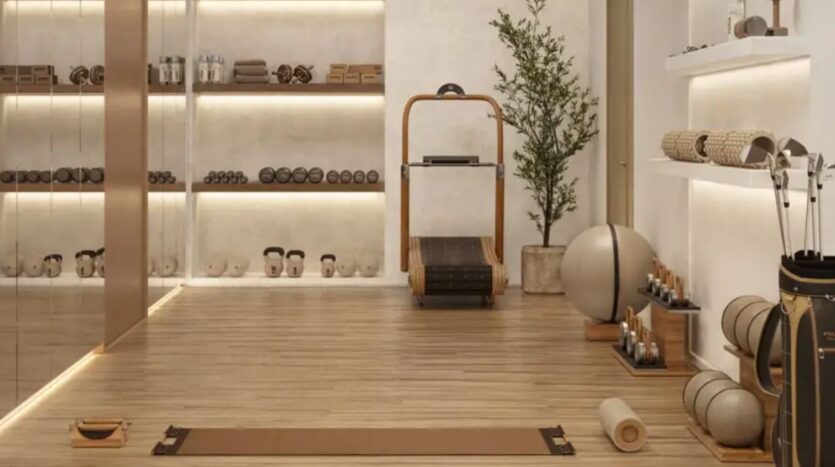 Salle de sport minimaliste à Hudayriyat Golf Estates avec sols en bois, tapis de yoga, ballons de fitness, tapis de course, haltères, rouleaux en mousse, kettlebells, étagères bien rangées pour l'équipement, et touches de verdure pour un espace d'entraînement serein.