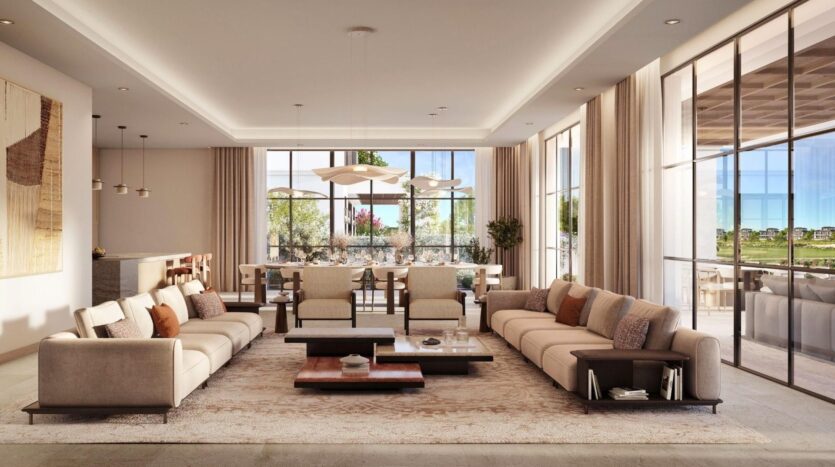 Salon spacieux et moderne à Hudayriyat Golf Estates avec deux canapés beiges, des tables basses et de grandes fenêtres laissant entrer la lumière naturelle. La salle à manger et la verdure extérieure complètent les couleurs neutres et le décor contemporain de l'ensemble.
