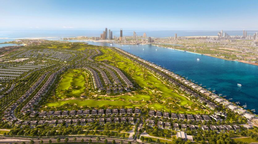 Vue aérienne d'une grande ville au bord de l'eau, avec Hudayriyat Golf Estates, des parcs verdoyants, des zones résidentielles et des gratte-ciel au loin, bordée par une baie et la mer, sous un ciel bleu clair.