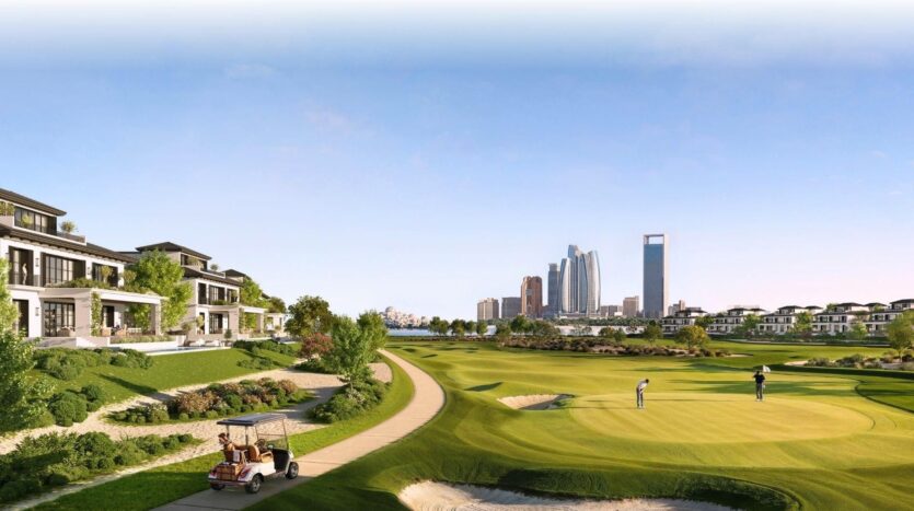 Un parcours de golf pittoresque à Hudayriyat Golf Estates montre deux personnes sur un green, entourées de maisons modernes et de verdure luxuriante. Une voiturette de golf suit un chemin tandis qu'une ligne d'horizon de la ville avec de grands bâtiments s'élève à l'arrière-plan sous un ciel clair.