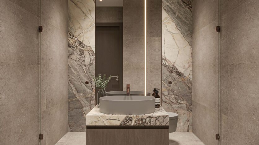 Salle de bains moderne avec des murs en pierre beige, un grand accent en marbre derrière le lavabo, une vasque ronde grise sur un meuble-lavabo en marbre, et un éclairage vertical doux par un grand miroir - élégamment stylé avec Oxford Cove d'Iman.