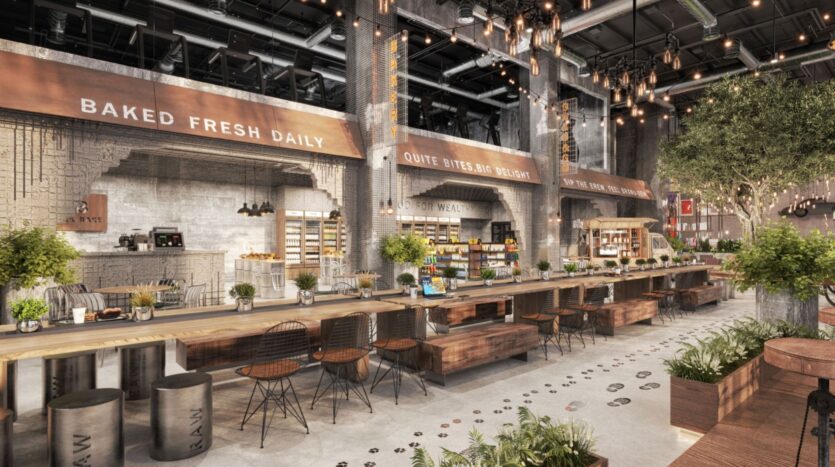 Café moderne de style industriel, Raw District by Imtiaz propose de longues tables en bois, des chaises en métal, des lampes suspendues, des plantes d'intérieur et des présentoirs de pâtisseries. Les panneaux indiquent "BAKED FRESH DAILY" et "QUIET BITES ARE DELIGHTFUL".