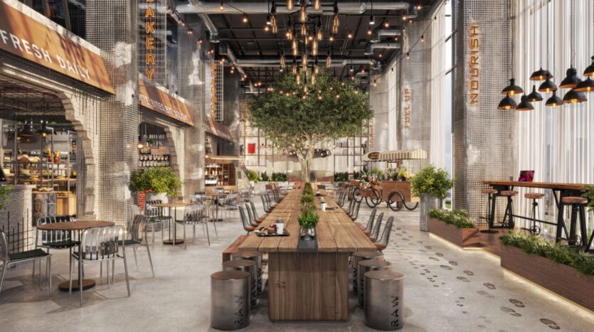 Un café moderne et spacieux, le Raw District by Imtiaz, présente de hauts plafonds, des tuyaux apparents, de grandes fenêtres et des lampes suspendues. Sa table commune en bois, ses plantes en pot et ses sièges variés créent une ambiance urbaine et accueillante.