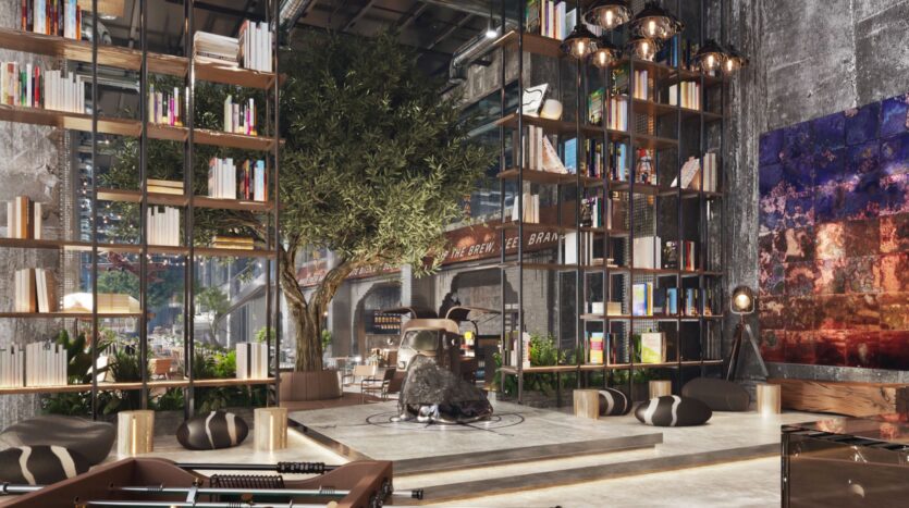 Le salon moderne et spacieux du Raw District by Imtiaz comprend de hautes étagères, un arbre d'intérieur, des poufs et un mélange de décoration industrielle et chaleureuse. De grandes fenêtres inondent l'espace de lumière, mettant en valeur les plantes vibrantes et les œuvres d'art colorées sur les murs en béton.