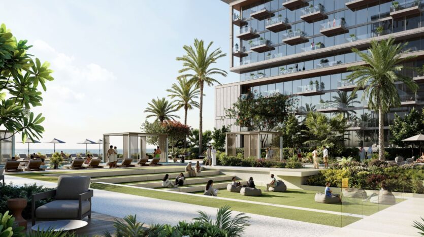 Un espace moderne de détente en plein air avec de l'herbe, des palmiers et des gens qui se prélassent. À côté, Raw District by Imtiaz propose un bâtiment aux parois de verre avec des balcons et des cabanons qui donnent sur une piscine ensoleillée ou sur la plage.