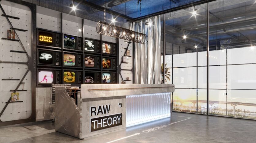 L'espace d'accueil moderne et industriel de Raw District by Imtiaz comprend un bureau en béton portant l'inscription "RAW THEORY", des étagères éclairées avec des plantes et des objets de décoration, des téléviseurs rétro fixés au mur, des lampes suspendues et de grandes baies vitrées.