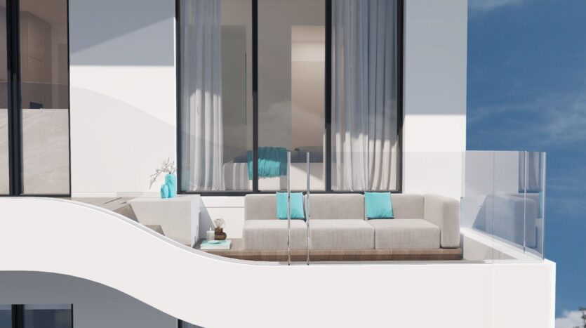 Un balcon moderne avec des balustrades en verre présente un canapé gris clair Reef 996 avec des coussins turquoise, une petite table avec un vase, et des fenêtres allant du sol au plafond drapées de rideaux gris. La scène est lumineuse et minimaliste.