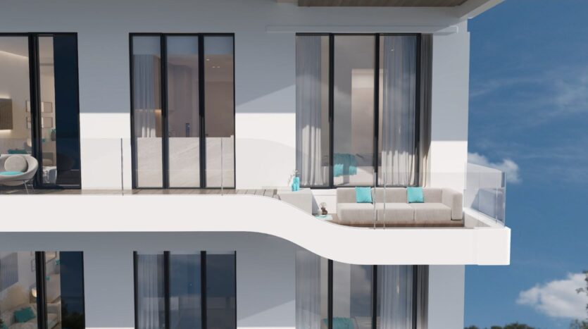 Le Reef 996, un immeuble d'appartements moderne et blanc, est doté de grandes baies vitrées allant du sol au plafond et d'un balcon incurvé où l'on trouve un canapé d'extérieur beige avec des coussins turquoise et une élégante balustrade en verre.